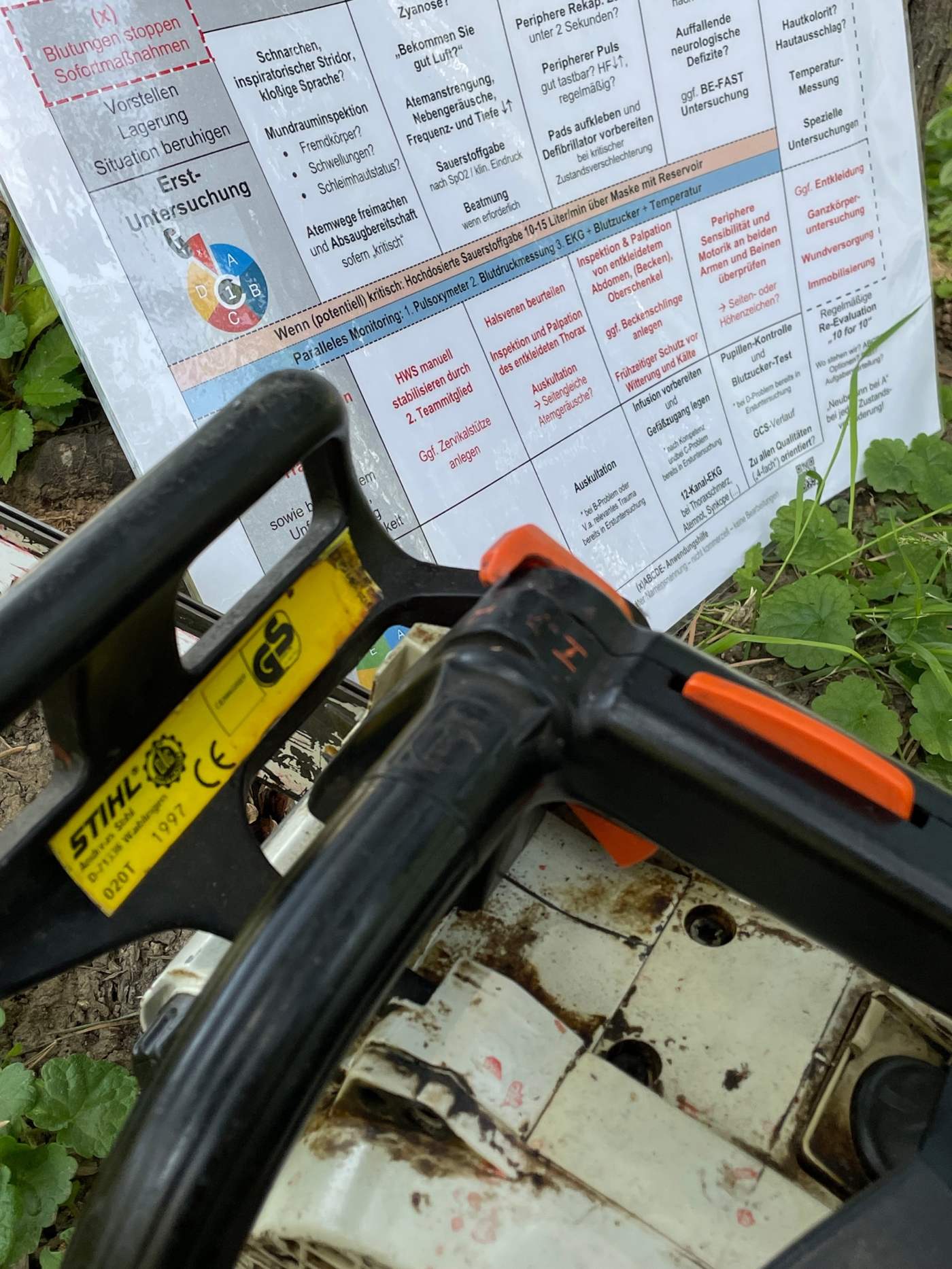 Die xABCDE-Anwendungshilfe liegt im Gras neben einer Motorsäge